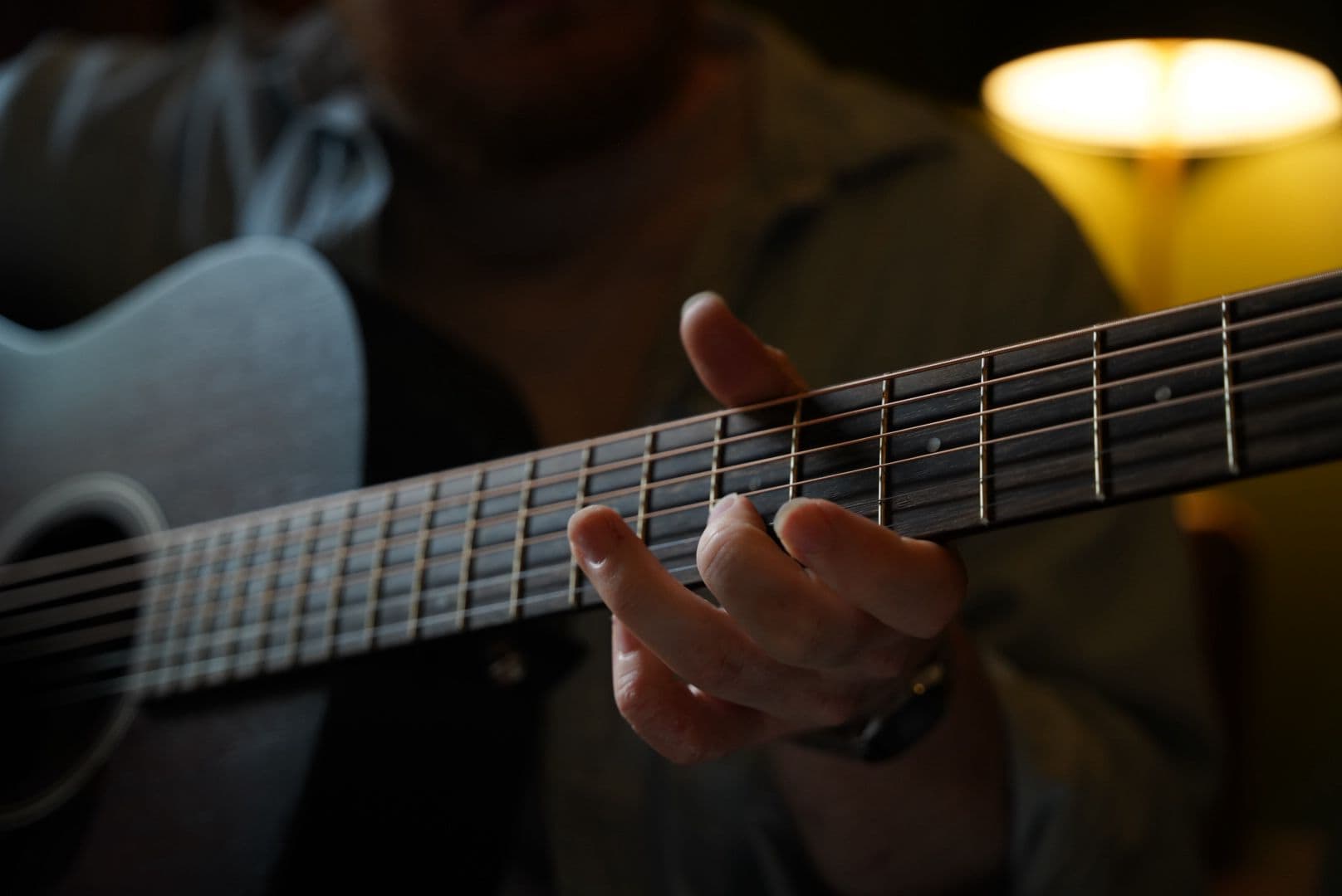 Close-up of a hand on the fretboard of an acoustic guitar in warm lamp light